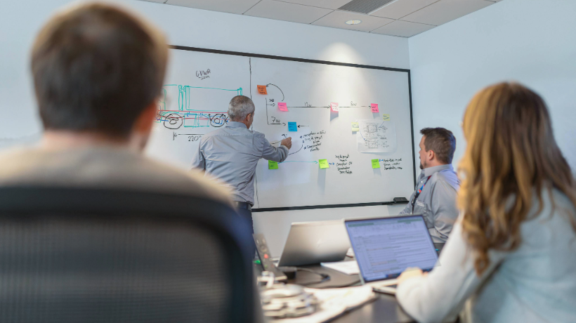 A team of engineers and project managers collaborating in a conference room, reviewing timelines and strategizing to keep their product development project on track.