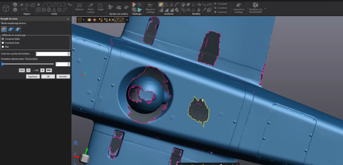 Un écran d'ordinateur affiche un logiciel de modélisation 3D avec une vue rapprochée d'un composant structurel, faisant partie d'un avion. Le modèle présente des zones mises en évidence en rose et en jaune, indiquant des zones d'intérêt ou de modification. Diverses options d'outils sont visibles.